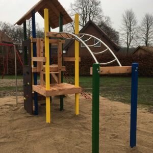 Bunter Spielturm auf einem Sandspielplatz, im Hintergrund sind Häuser und winterkahle Bäume zu sehen.