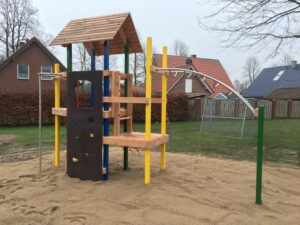 Spielplatz mit Klettergerüst und Rutsche auf Sandfläche, umgeben von Rasen und Wohnhäusern.