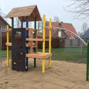 Spielplatz mit Klettergerüst und Rutsche auf Sandfläche, umgeben von Rasen und Wohnhäusern.