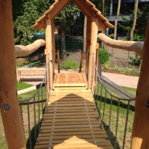 Holz-Hängebrücke mit Geländern, die zu einem kleinen Pavillon in einem bewaldeten Park führt.