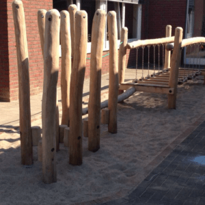 Holzspielplatzgerät mit Balancierseilen und Sandboden, umgeben von einem Pflasterweg.